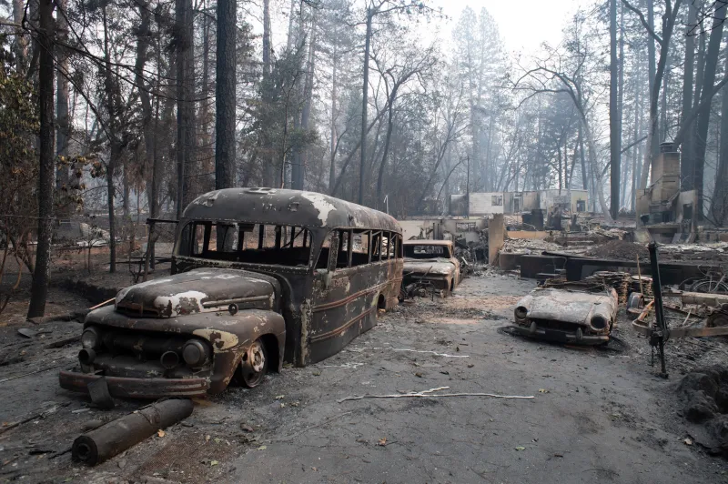 A very old bus and cars destroyed by fire. This appears to not have been traffic but someone's old collection in front of their house.